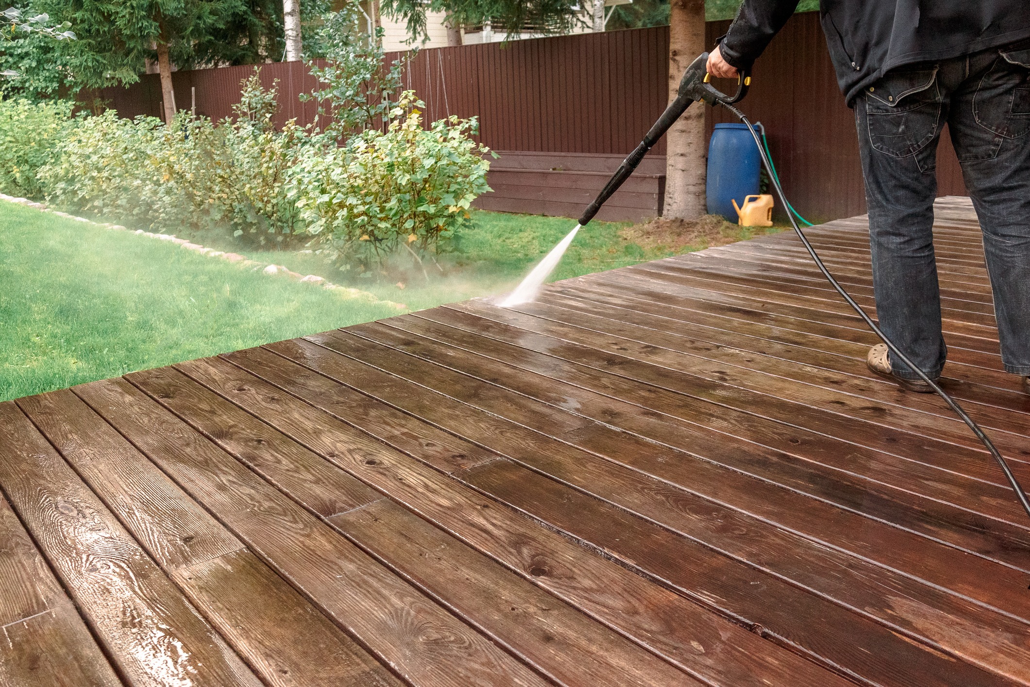 A cleaning technician pressure washes a wooden deck.