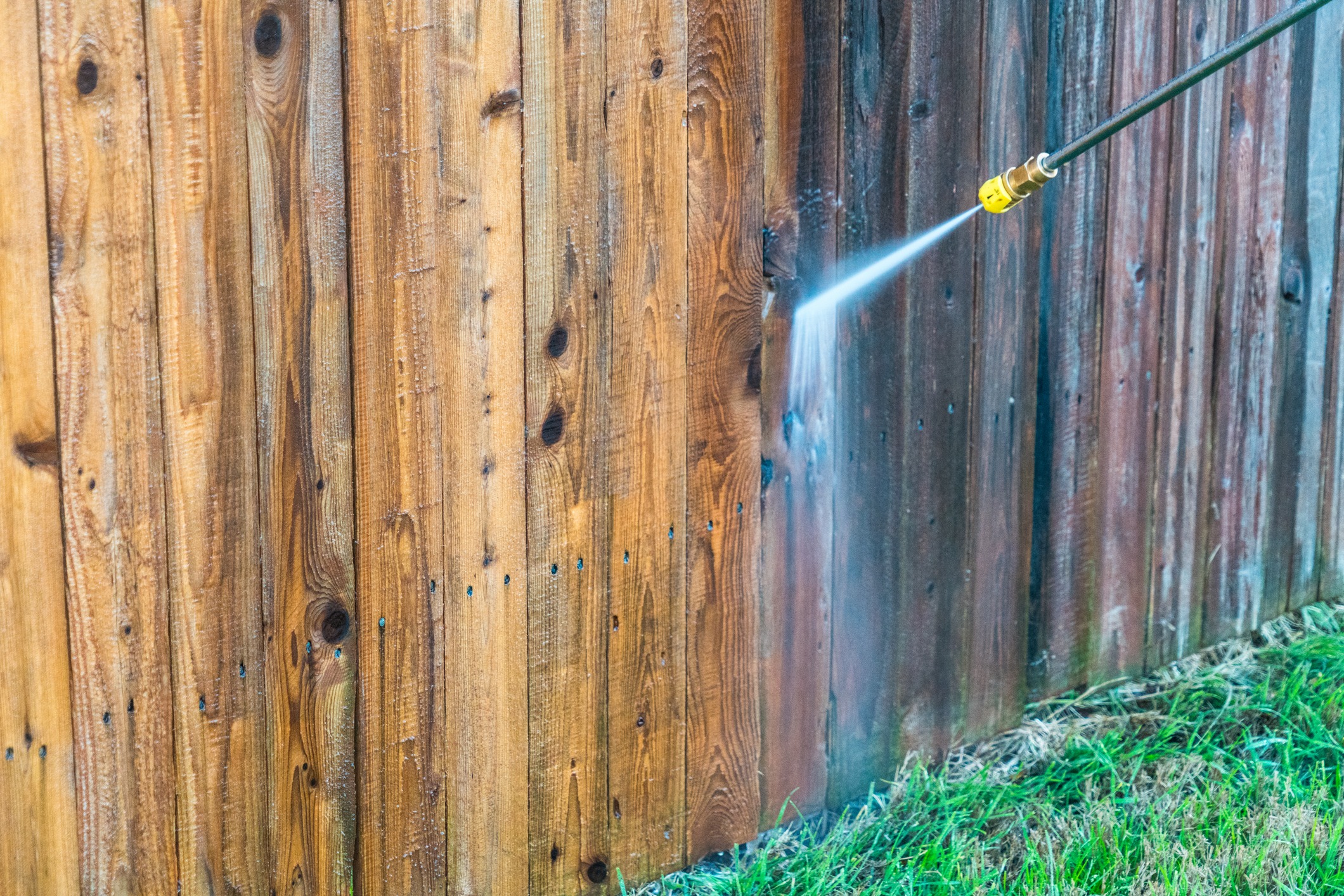 A cleaning technician pressure washes a wooden fence.